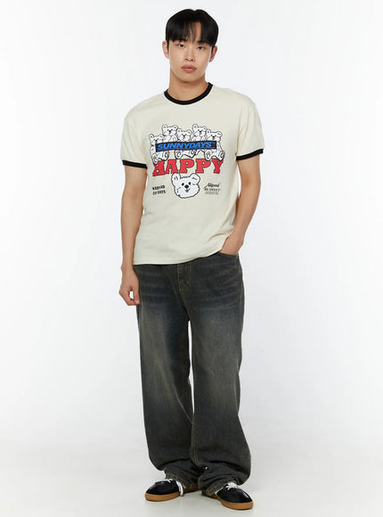 Men's Graphic T-Shirt IU529 Light beige front full-body view on male model one hand in pocket relaxed stance black ringer trim HAPPY bear print styled with dark wide-leg jeans