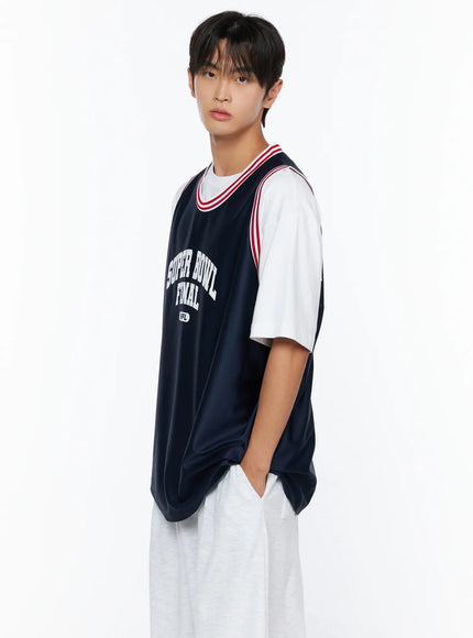 Men's Graphic Varsity Jersey IL515 Dark blue side-angle shot on male model with hand in pocket, showing oversized silhouette and layered white tee underneath