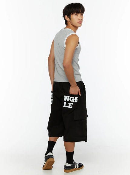 Men's Graphic Wide Jorts IL510 Black three-quarter back side view on male model in grey tank top, hand in pocket, NGLE LE print visible