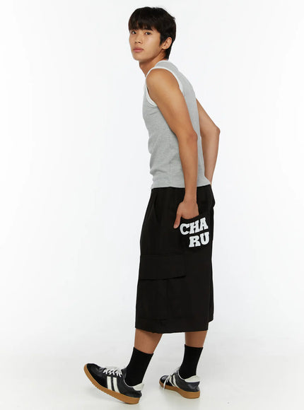 Men's Graphic Wide Jorts IL510 Black full-length front view on male model in grey tank top, hands in pockets, relaxed wide-leg silhouette