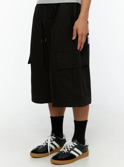 Men's Graphic Wide Jorts IL510 Black right side view on model showing deep cargo pocket and partial CHA RU graphic print detail