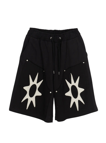 Men's Happy Sun Jorts IL510 Black flat-lay front view showing elastic drawstring waistband, dual cream textured sun appliqué patches and silver snap hardware