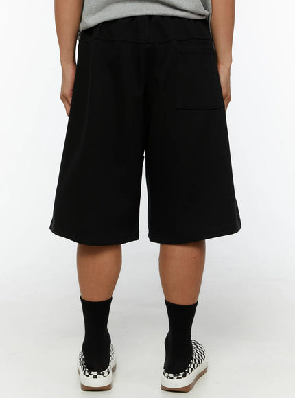 Men's Happy Sun Jorts IL510 Black full front styling shot on male model with black sleeveless top, hands in pockets, dual cream sun patches prominent