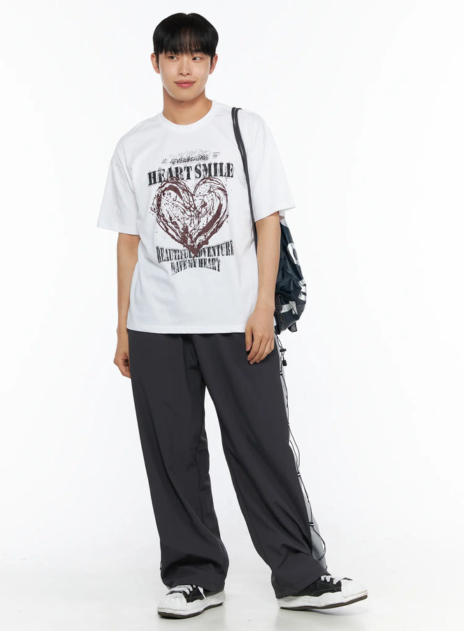 LEWKIN Men's Heart Graphic Tee IL514 White front shot on male model in 3/4 pose wearing dark track pants and carrying bag, oversized cotton tee with grunge heart print