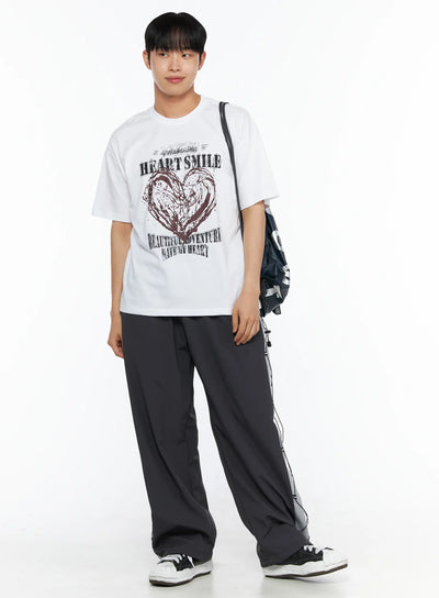 LEWKIN Men's Heart Graphic Tee IL514 White front shot on male model in 3/4 pose wearing dark track pants and carrying bag, oversized cotton tee with grunge heart print
