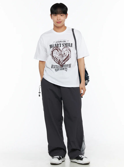 Men's Heart Graphic Tee IL514 White full-body front shot on smiling male model styled with dark wide-leg pants and crossbody bag, relaxed oversized streetwear fit