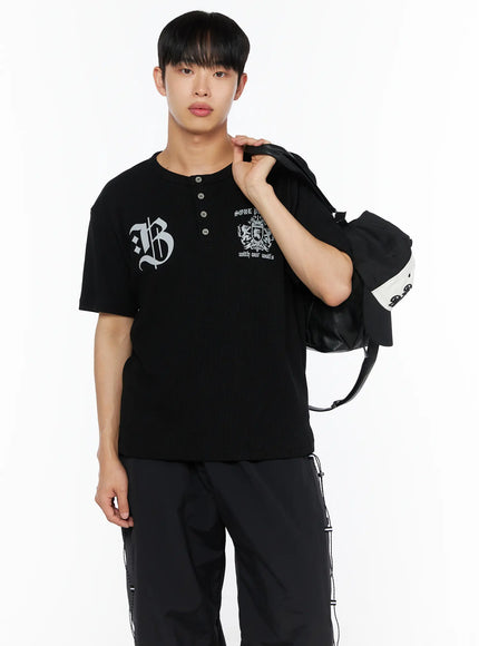 LEWKIN Men's Henley Waffle Tee IL514 Black M/L front shot on male model holding leather bag over shoulder with gothic B and crest graphic print