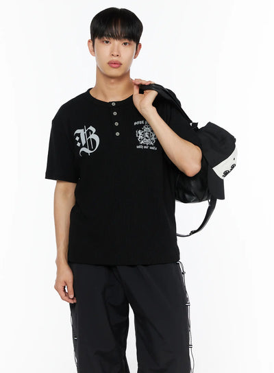 LEWKIN Men's Henley Waffle Tee IL514 Black M/L front shot on male model holding leather bag over shoulder with gothic B and crest graphic print