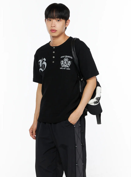 Men's Henley Waffle Tee IL514 Black side shot on male model carrying leather bag on shoulder with gothic B crest graphic and henley button detail