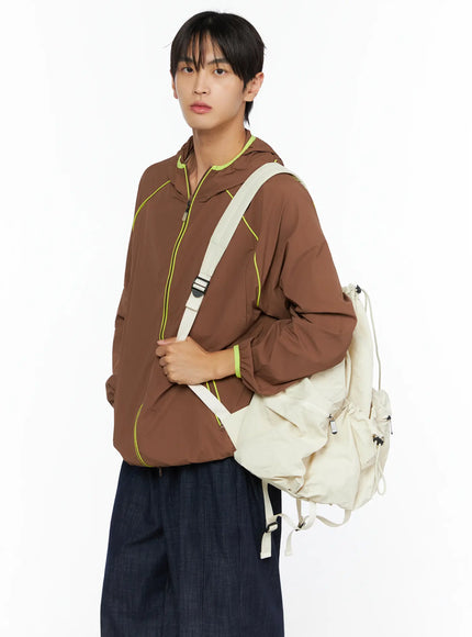 LEWKIN Men's Hooded Windbreaker IL528 Brown M/L three-quarter shot on model carrying cream backpack, neon yellow piping and hood trim, lightweight nylon
