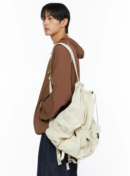 Men's Hooded Windbreaker IL528 Brown side shot on model carrying large cream drawstring backpack, neon yellow piping along back seam