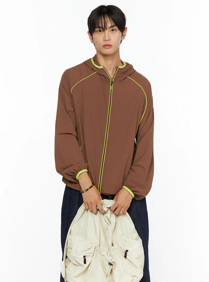 Men's Hooded Windbreaker IL528 Brown front shot on model holding cream bag, neon yellow zip and cuff trim, paired with wide-leg dark denim