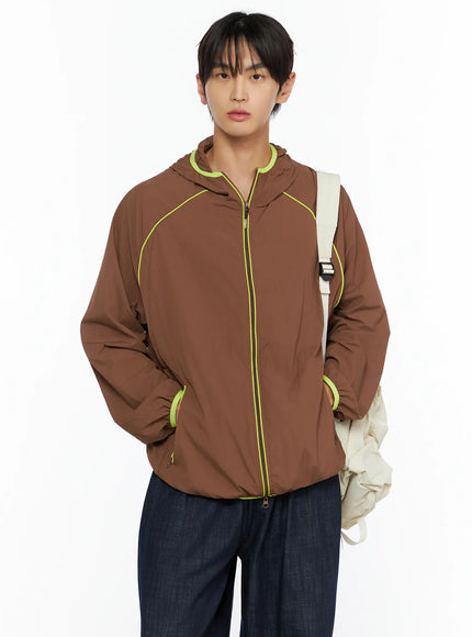 Men's Hooded Windbreaker IL528 Brown front shot on model with cream backpack slung on shoulder, neon yellow zip trim, hands in pockets