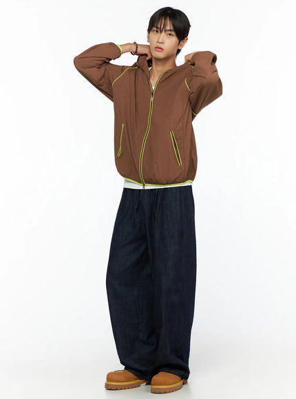 Men's Hooded Windbreaker IL528 Brown full-body front shot on model hands raised adjusting hood, neon yellow zip pocket and hem trim visible