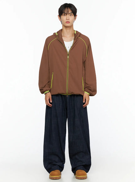 Men's Hooded Windbreaker IL528 Brown full-body front shot on model, zip closed, neon yellow seam piping visible, layered over white tee
