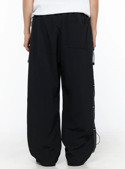 Men's Lace-Up Track Pants (Black) IL514 Black back-view close-up on model showing rear pocket, elastic waistband, and side lace-up panel with cord hardware
