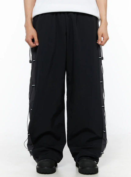 LEWKIN Men's Lace-Up Track Pants (Black) IL514 Black M/L front close-up on model showing wide-leg silhouette, elastic waistband, and side cord lace-up panel detail