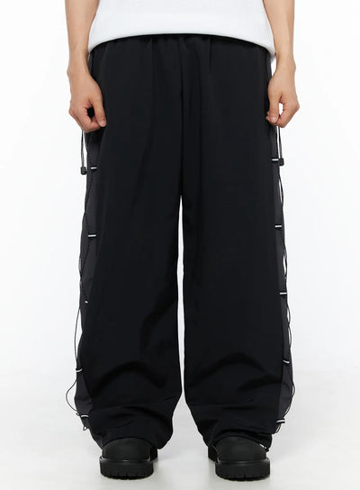 LEWKIN Men's Lace-Up Track Pants (Black) IL514 Black M/L front close-up on model showing wide-leg silhouette, elastic waistband, and side cord lace-up panel detail