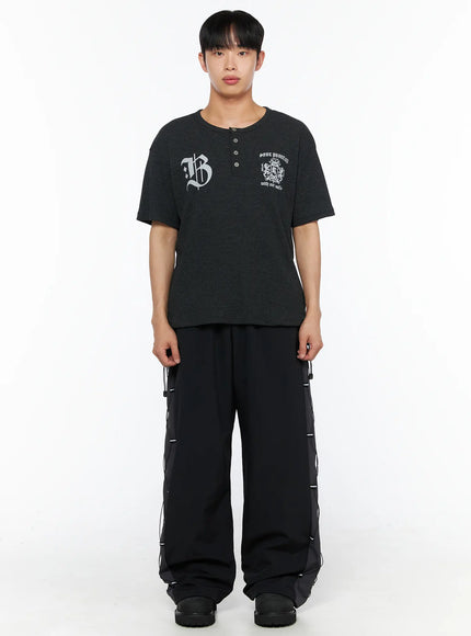 Men's Lace-Up Track Pants (Black) IL514 Black full-length front shot on male model wearing dark henley tee, arms relaxed, showing wide-leg fit and lace-up side panels
