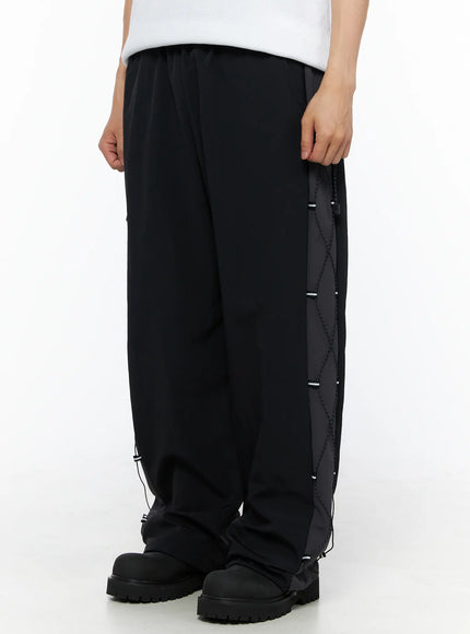 Men's Lace-Up Track Pants (Black) IL514 Black side close-up on model highlighting diamond cross-lace cord panel with reflective toggles along outer leg seam