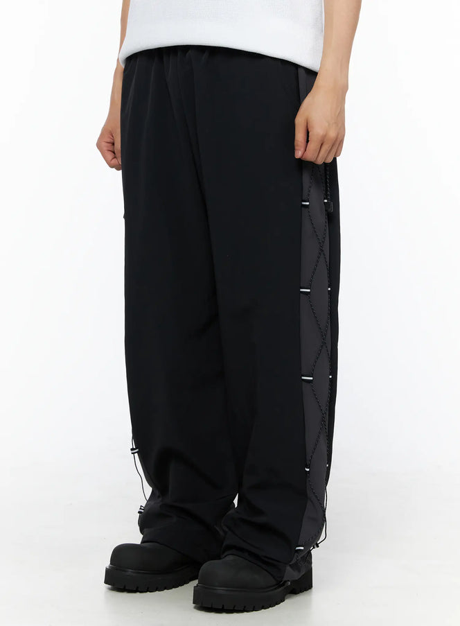 Men's Lace-Up Track Pants (Black) IL514 Black side close-up on model highlighting diamond cross-lace cord panel with reflective toggles along outer leg seam