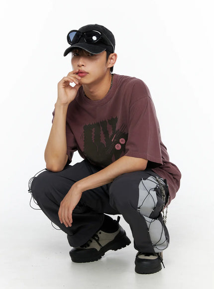 Men's Lace-Up Track Pants (Dark Gray) IL514 dark gray crouching pose shot on model in burgundy tee and black cap, hand near chin, showing side lace-up and chain hardware detail