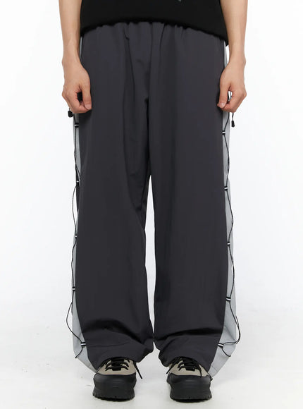 Men's Lace-Up Track Pants (Dark Gray) IL514 dark gray side shot on model standing with drawstring bag, showing reflective gray panel and lace-up cord detail