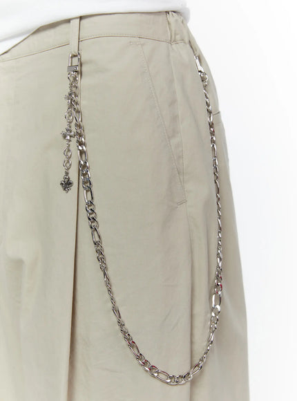 LEWKIN Men's Layered Cross Chain IL509 Silver close-up detail on beige trousers showing figaro chain draped across hip with cross and fleur-de-lis charms