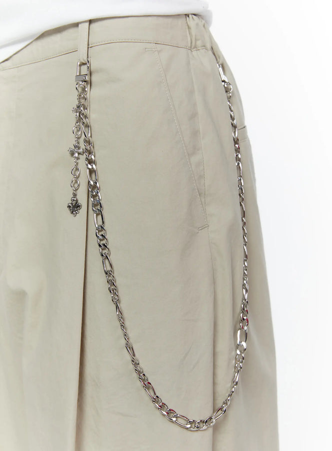 LEWKIN Men's Layered Cross Chain IL509 Silver close-up detail on beige trousers showing figaro chain draped across hip with cross and fleur-de-lis charms