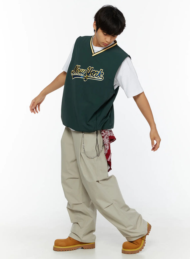 Men's Layered Cross Chain IL509 Silver full outfit side-angle on male model walking wearing green New York vest white tee beige wide-leg pants and boots