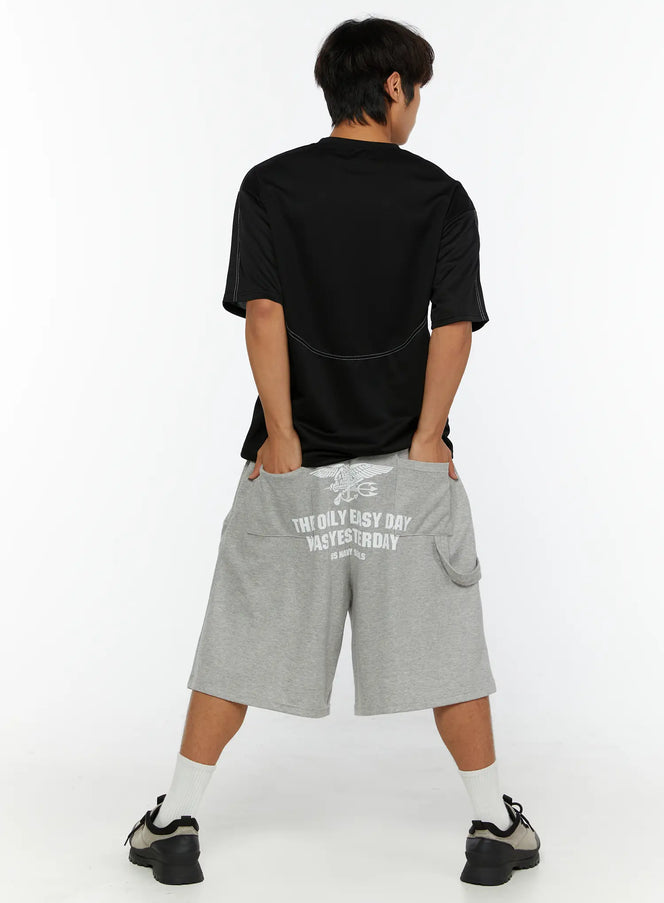 Men's Lettering Bermuda Shorts IL513 Gray back view on male model, white US Navy Seals eagle graphic print and lettering across seat, hands in pockets, black tee styling