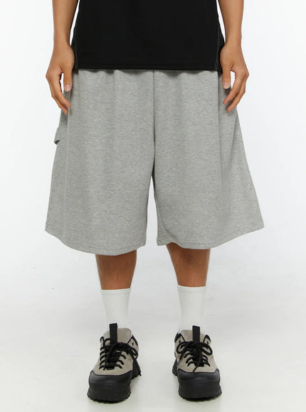 LEWKIN Men's Lettering Bermuda Shorts IL513 Gray M/L front close-up on model, heather gray cotton terry fabric, wide-leg silhouette, elastic waistband, styled with black tee and sneakers