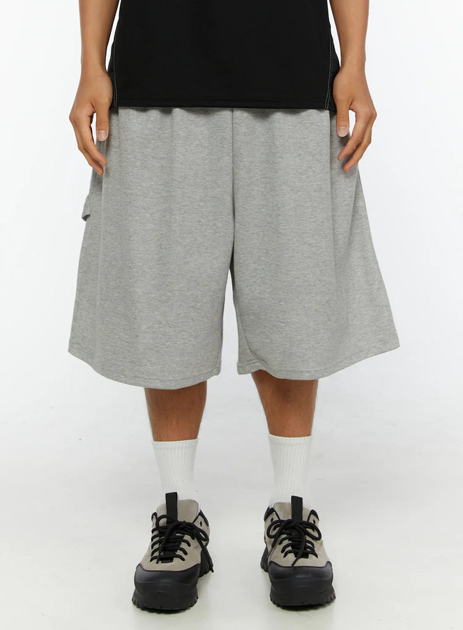 LEWKIN Men's Lettering Bermuda Shorts IL513 Gray M/L front close-up on model, heather gray cotton terry fabric, wide-leg silhouette, elastic waistband, styled with black tee and sneakers