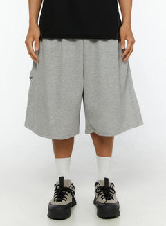 LEWKIN Men's Lettering Bermuda Shorts IL513 Gray M/L front close-up on model, heather gray cotton terry fabric, wide-leg silhouette, elastic waistband, styled with black tee and sneakers