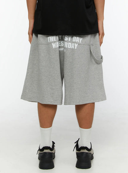 Men's Lettering Bermuda Shorts IL513 Gray back close-up on male model, white US Navy Seals eagle and lettering print across back waistband, wide-leg silhouette, sneakers and white socks