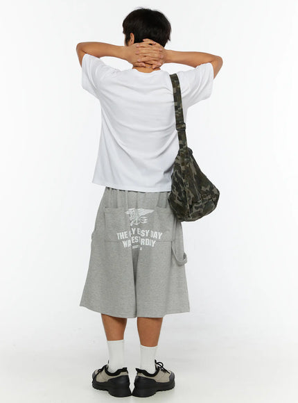 Men's Lettering Bermuda Shorts IL513 Gray back view on male model with arms raised, camo crossbody bag, white tee, US Navy Seals graphic print visible on back of shorts