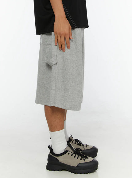 Men's Lettering Bermuda Shorts IL513 Gray side view on male model, visible cargo-style side pocket with tab detail, heather gray marl fabric, wide-leg cut, sneakers and white socks
