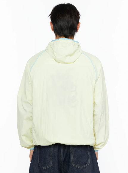 Men's Lightweight Windbreaker IL528 Light yellow back view on model showing hood, raglan seams with blue contrast piping, relaxed fit