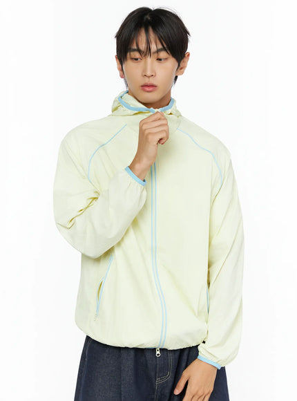 Men's Lightweight Windbreaker IL528 Light yellow front close-up crop on model showing zip closure, hood, and blue contrast stitching