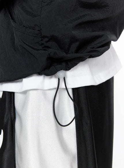 Men's Lightweight Windbreaker Jacket IL515 Black close-up detail of elasticated hem with adjustable drawcord stopper showing crinkle nylon texture and layered styling