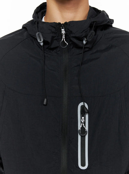 Men's Lightweight Windbreaker Jacket IL515 Black close-up detail of hood collar area showing reflective zipper pull chest pocket and drawstring stopper hardware
