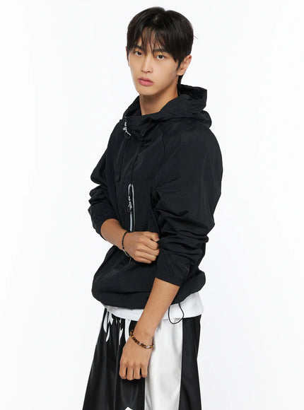 Men's Lightweight Windbreaker Jacket IL515 Black side shot on male model with hands clasped at chest showing hood drawstring and reflective zipper pocket