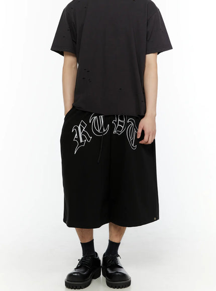 Men's Logo Embroidered Snap Hem Bermuda Sweat Shorts (Black) IL507 back view on model standing straight showing clean plain reverse and drawstring waist with derby shoes