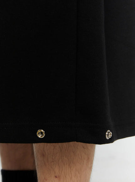 Men's Logo Embroidered Snap Hem Bermuda Sweat Shorts (Black) IL507 close-up detail of gold and silver metal snap buttons at the hem of wide-leg black fabric
