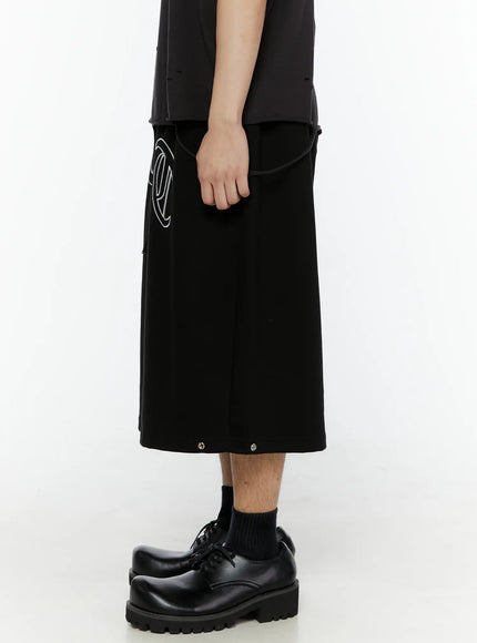 Men's Logo Embroidered Snap Hem Bermuda Sweat Shorts (Black) IL507 side view on model showing extended length silhouette with drawstring waist and snap buttons at hem