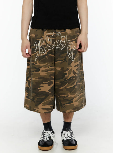 Men's Logo Embroidered Snap Hem Bermuda Sweat Shorts (Camouflage) IL507 Camouflage close-up detail of old-English embroidered lettering on camouflage cotton fabric with elastic waistband visible at top