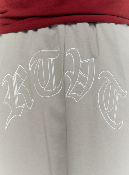 Men's Logo Embroidered Snap Hem Bermuda Sweat Shorts (Gray) IL507 gray close-up detail of old-English embroidered logo on front waistband area on model