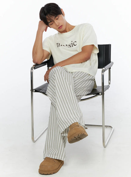 LEWKIN Men's Music Print T-Shirt IL515 ivory seated lifestyle shot male model resting head on hand on black metal chair wearing striped wide-leg pants