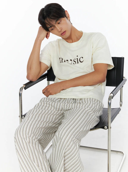 Men's Music Print T-Shirt IL515 ivory seated close-up lifestyle shot male model resting cheek on hand looking down showing music graphic chest print detail