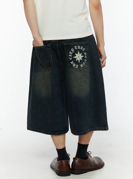 Men's 'Never Stop' Graphic Bermuda Jorts (Blue) IL507 back close-up on model, showing star compass graphic with old english circular text on right back pocket, washed denim texture